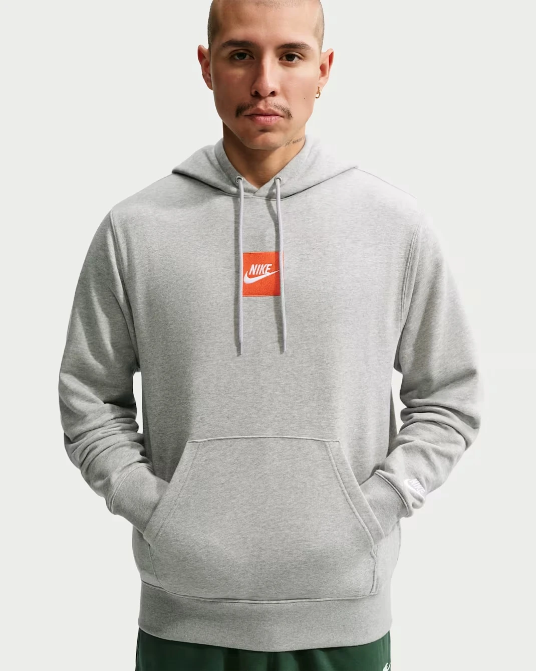 Nike Sportswear Club French Terry Hoodie in heather grey with orange Nike logo.
