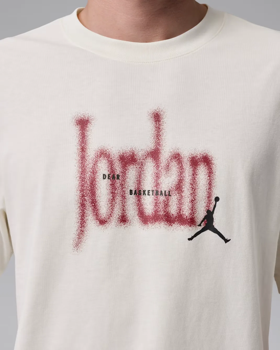 Close-up of the front graphic on the Jordan Brooklyn Love Letter T-Shirt in Soft Pearl featuring a Team Red spray-style Jordan logo and black Jumpman.