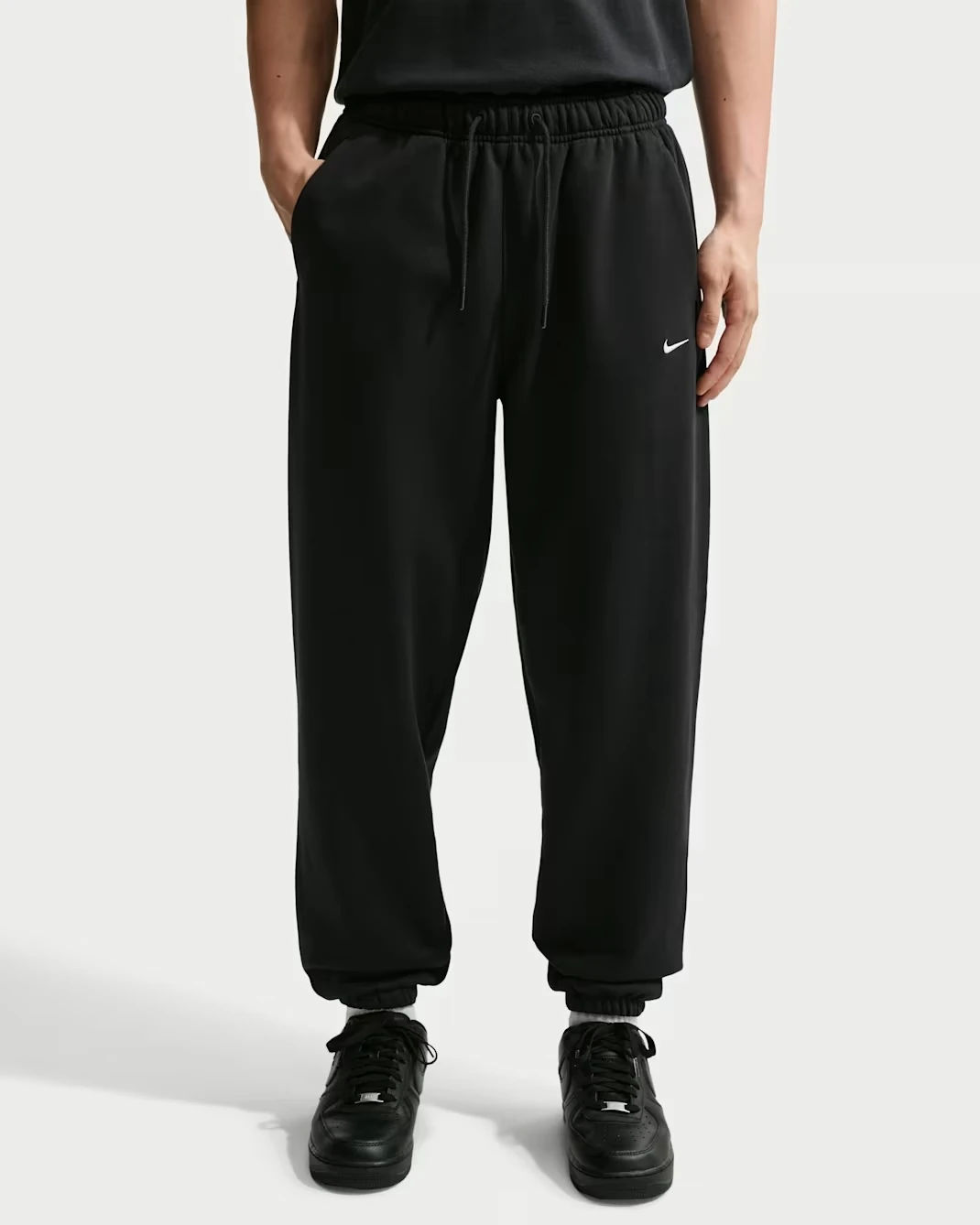 Nike Solo Fleece Men's Cuffed Pants in black featuring a white Swoosh logo.
