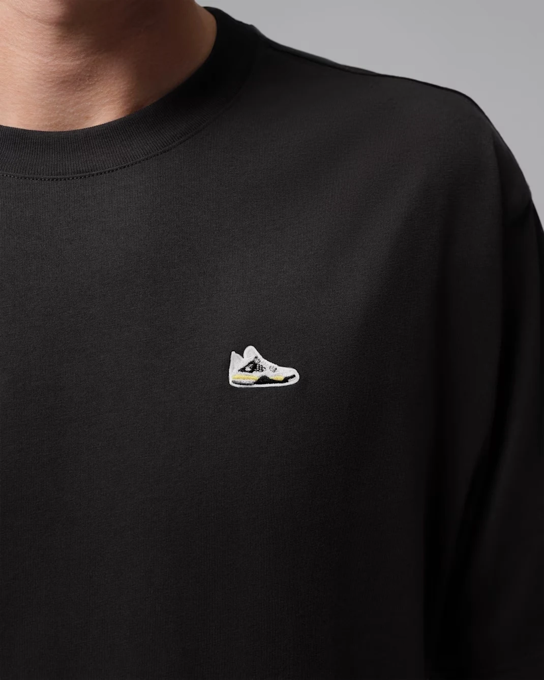 Close-up of black Jordan T-shirt with white, black and Tour Yellow sneaker patch.