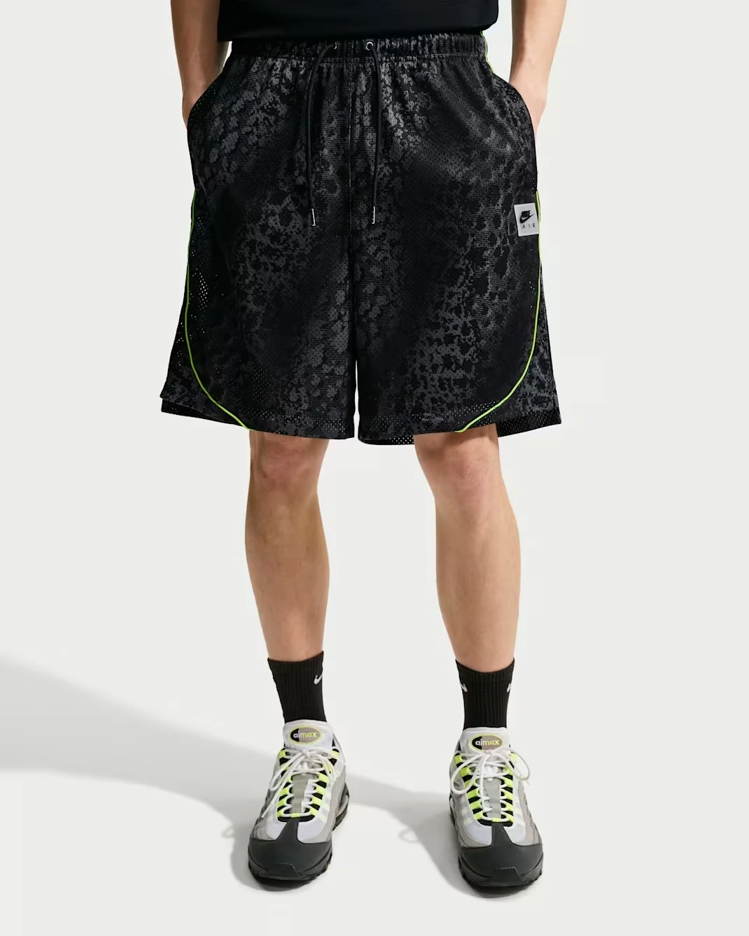 Model wearing Nike Air All-Over Print Mesh Shorts in Black, Anthracite and Neon Yellow with Nike Air Max sneakers.