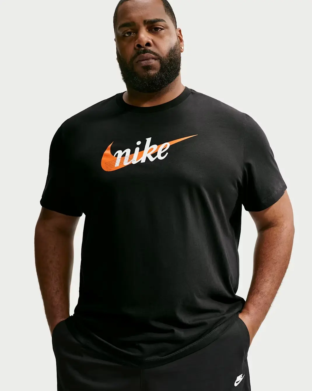 Model wearing the Nike Sportswear T-Shirt in black with white Nike lettering and a Starfish orange Swoosh