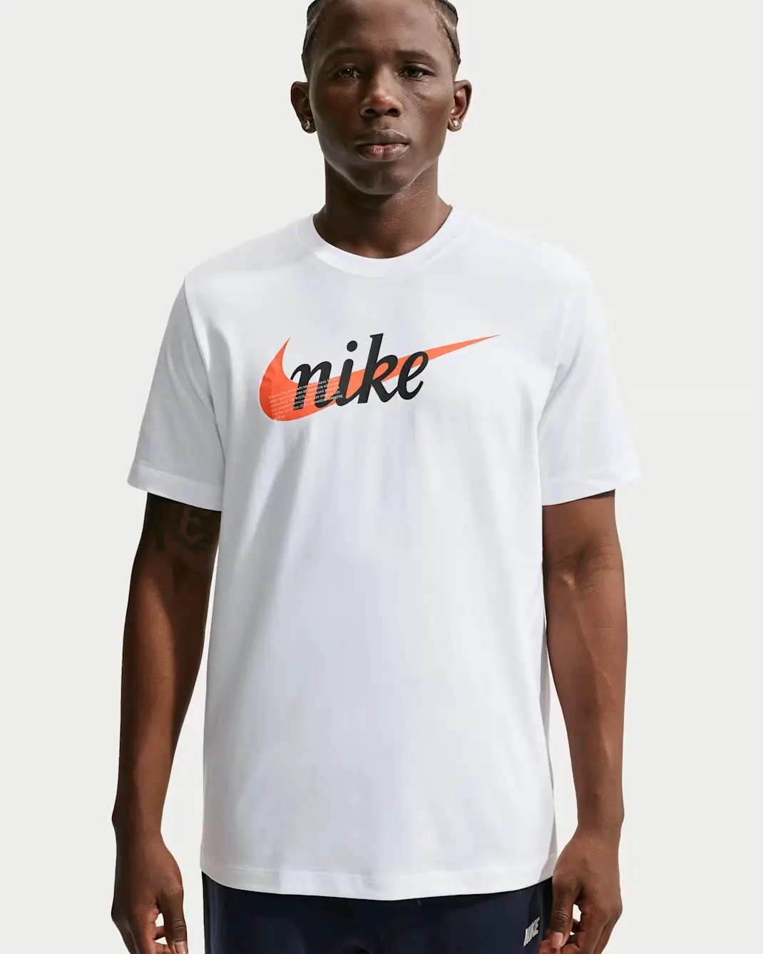Model wearing the Nike Sportswear T-Shirt in white with black Nike lettering and a Starfish orange Swoosh