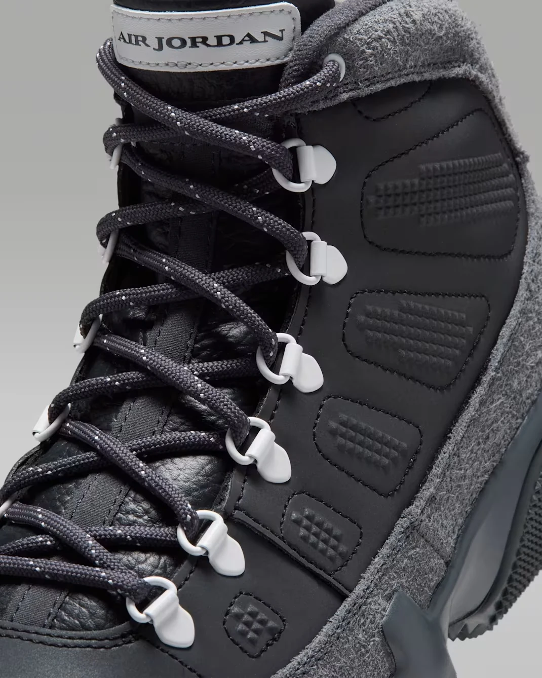 Close-up of the Air Jordan 9 Retro Boot Anthracite Reflective showing dark patterned laces, white lace hooks and textured side panels.