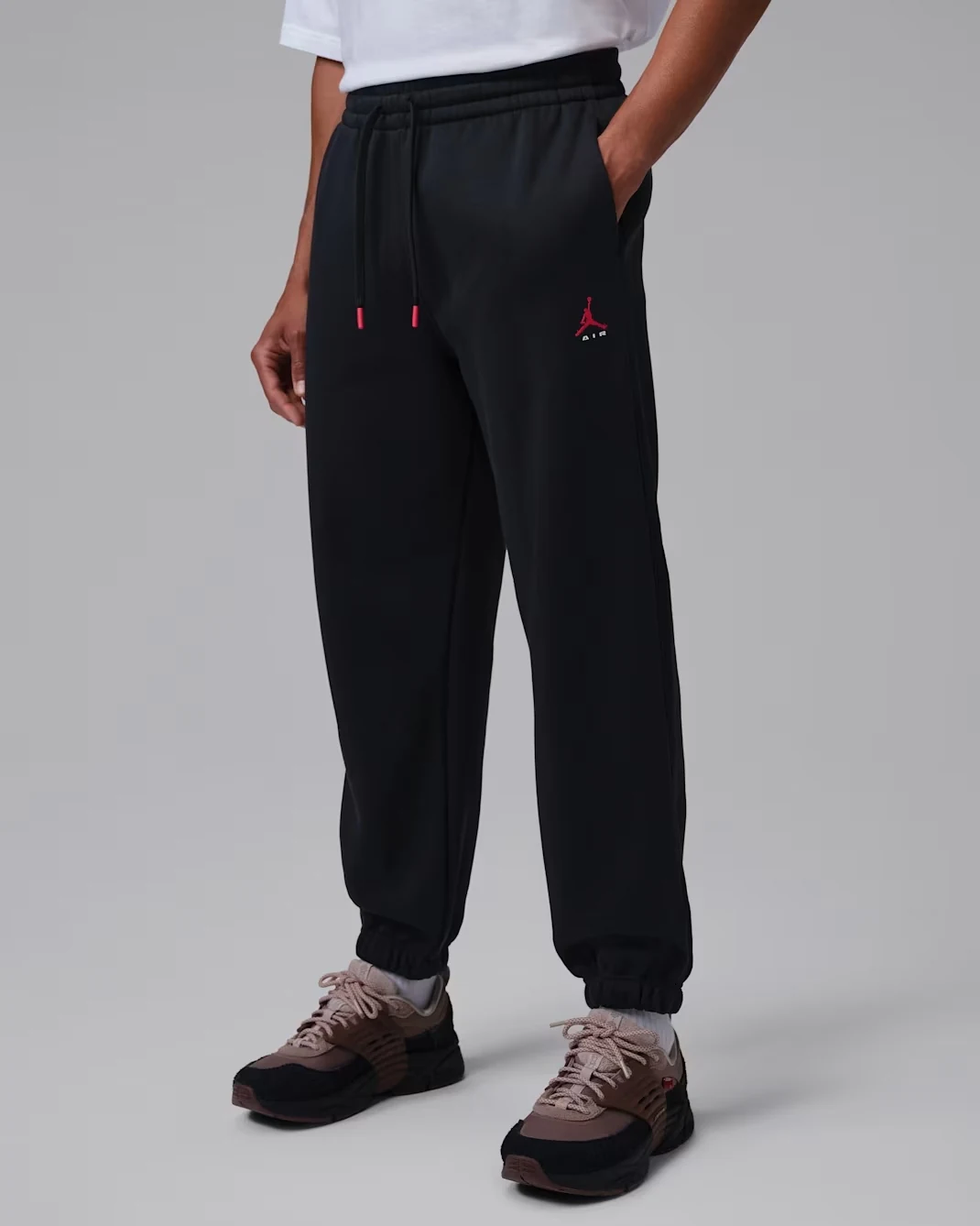 Model wearing black Jordan Brooklyn Fleece Cuffed Pants with red Jumpman logo, red-tipped drawstrings and elastic ankle cuffs.