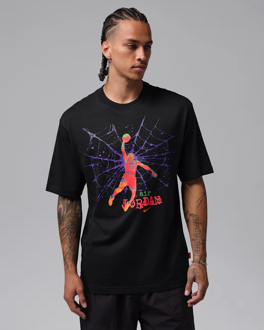 Model wearing a black Jordan Brooklyn T-shirt featuring purple spiderweb graphics, a colorful Michael Jordan dunk illustration and orange and green accents.