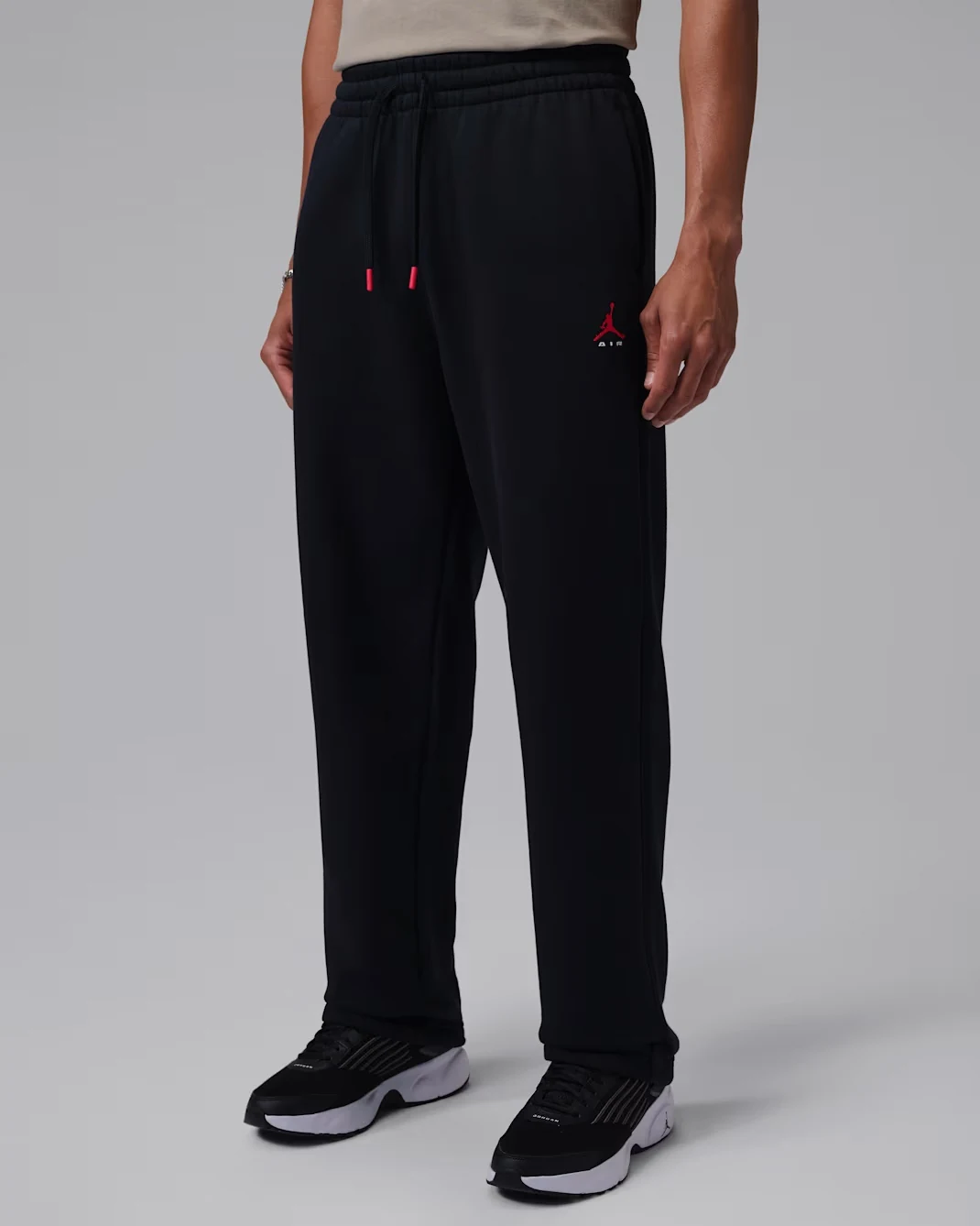 Model wearing black Jordan Brooklyn Statement Fleece Open-Hem Pants with red Jumpman logo, red-tipped drawstrings and relaxed straight-leg fit.