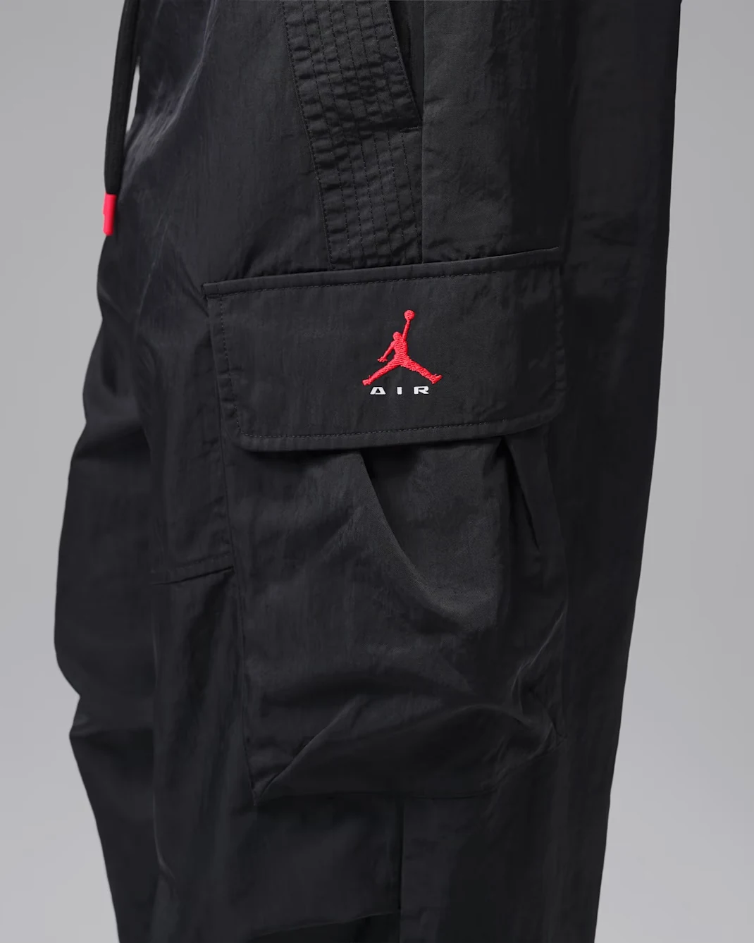 Close-up of black Jordan Brooklyn Woven Cargo Pants showing the cargo pocket with embroidered red Jumpman logo, white Air lettering and woven fabric details.