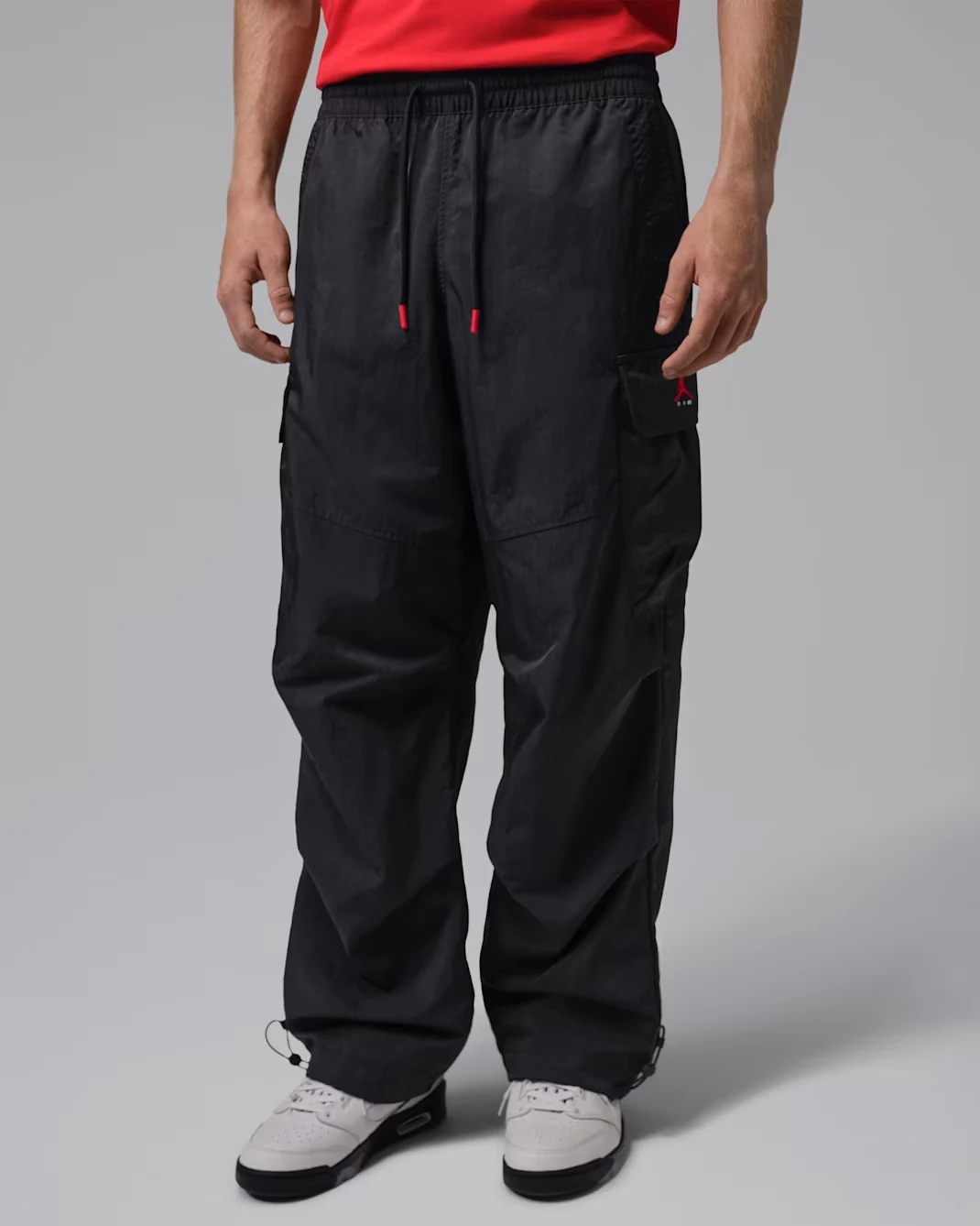 Model wearing black Jordan Brooklyn Woven Cargo Pants with red Jumpman logo, red-tipped drawstrings, cargo pockets and adjustable ankle hems.