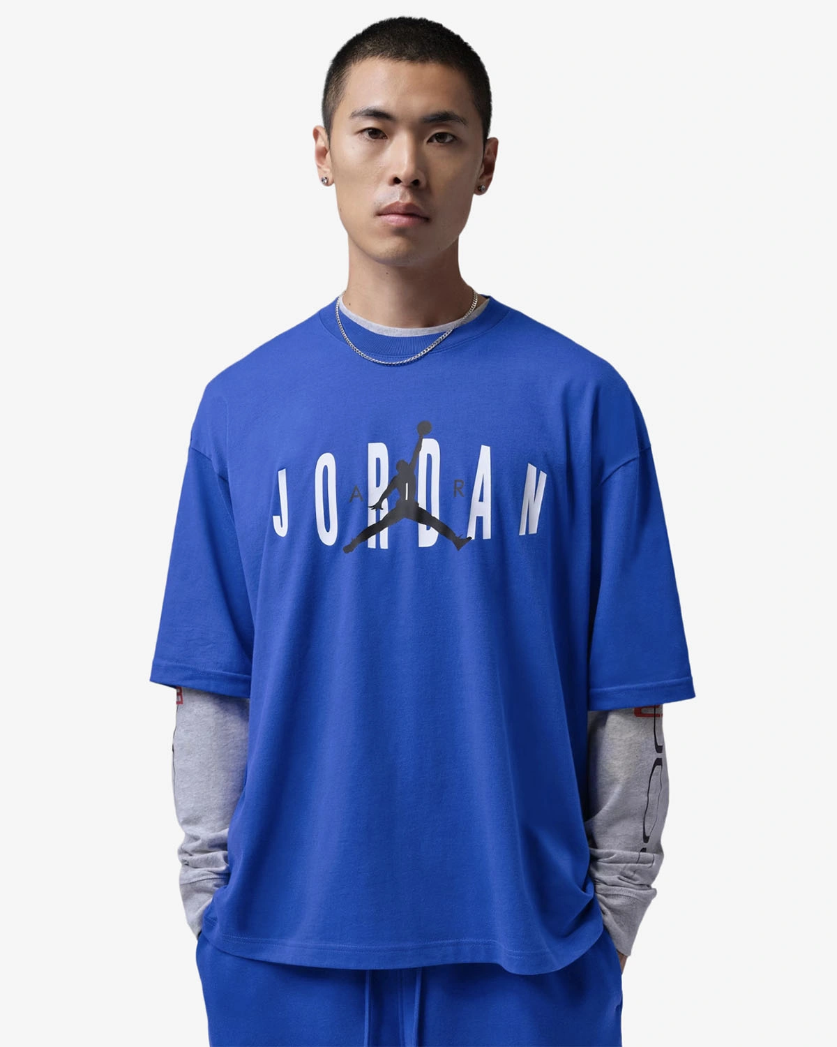Model wearing a royal blue Jordan Chest Stretch Oversized T-Shirt with white Jordan lettering and a black Jumpman logo over a gray long-sleeve shirt.