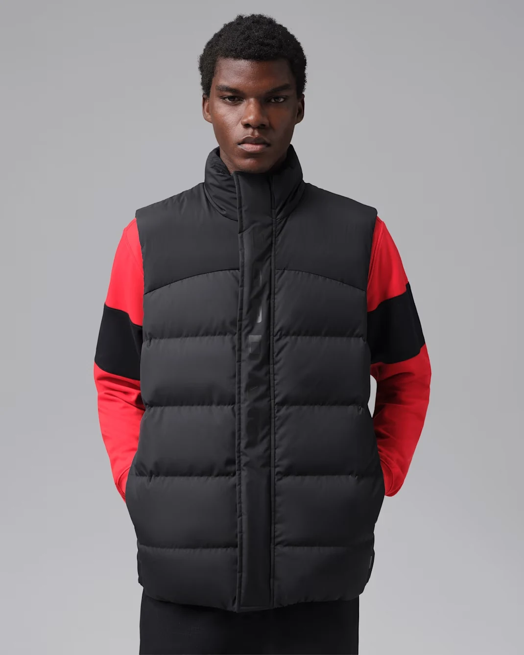 Model wearing a black Jordan Flight down vest over a red and black long-sleeve top.