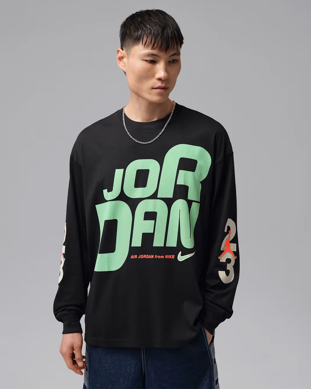 Model wearing a black Jordan Flight long-sleeve graphic T-shirt featuring oversized mint green Jordan lettering, orange Jumpman accents and cream-colored sleeve graphics.