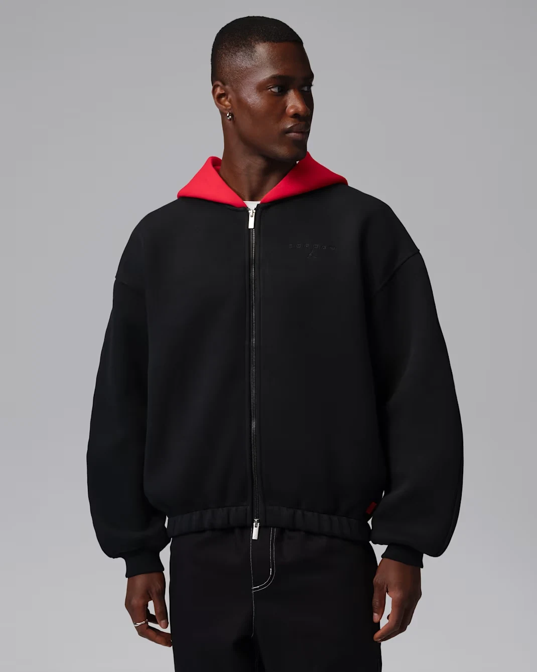 Model wearing a black Jordan Flight men's zip-up sweater with a contrasting red hood and full-length front zipper.