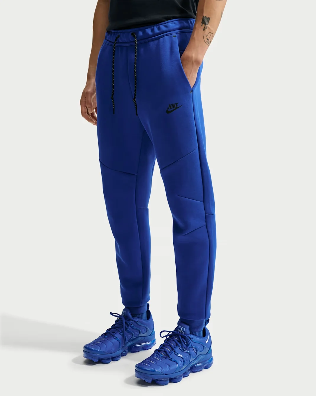 Royal blue Nike Tech Fleece joggers with tapered legs, black Nike logo, and drawstring waistband