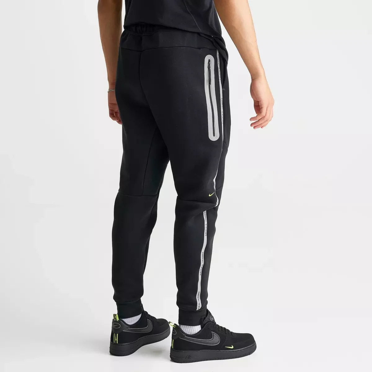 Nike Tech Fleece Reflective Jogger Pants in Black, Flat Pewter and Volt shown from the back with reflective zipper detailing and matching Nike sneakers.
